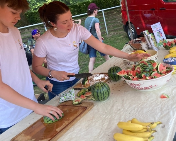 KI generiert: Menschen schneiden Wassermelonen und Bananen an einem Stand im Freien.