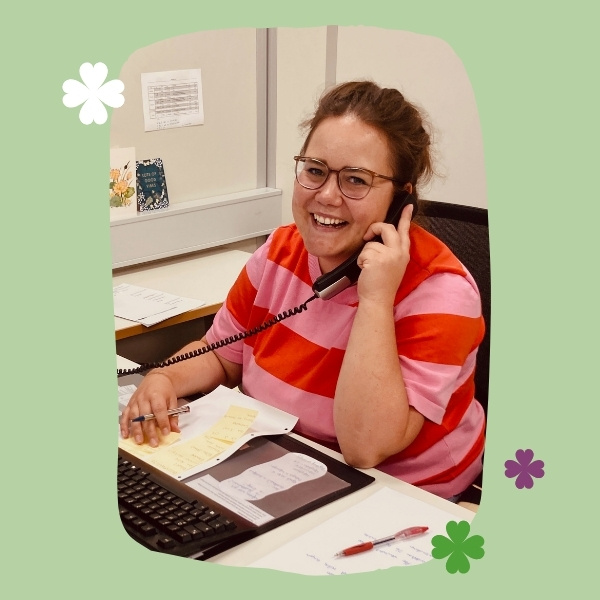 KI generiert: Eine Person telefoniert am Schreibtisch und lächelt. Dekoriert mit Blumen auf grünem Hintergrund.