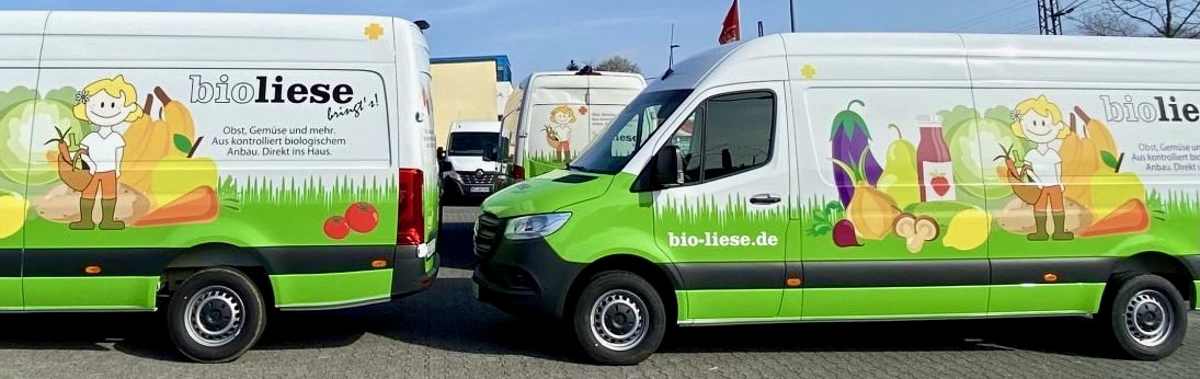 KI generiert: Zwei grüne Lieferwagen mit Bio-Liese-Werbung für frisches Obst und Gemüse. Text: "bio-liese.de".
