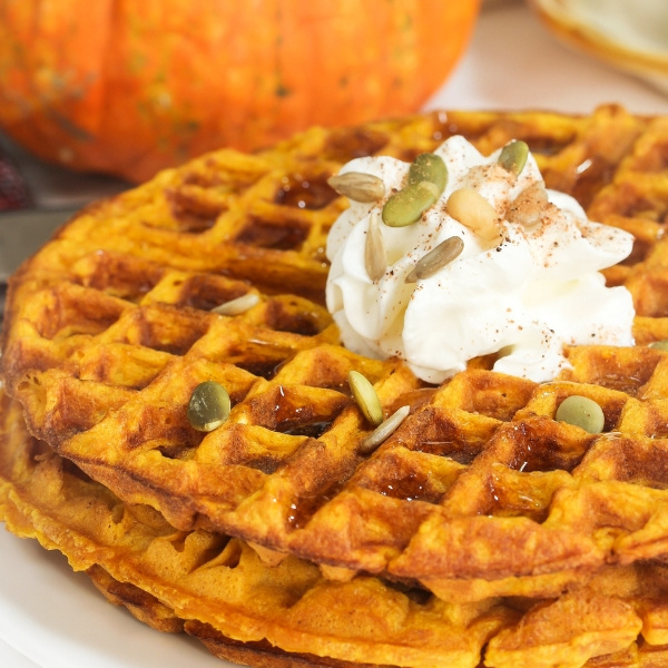 KI generiert: Kürbiswaffeln mit Sahne und Kernen. Hintergrund: Kürbis.