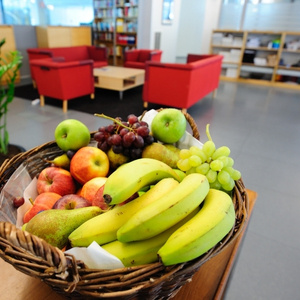 KI generiert: Ein Korb mit verschiedenen Früchten steht in einem modernen, gemütlichen Raum mit roten Stühlen im Hintergrund.