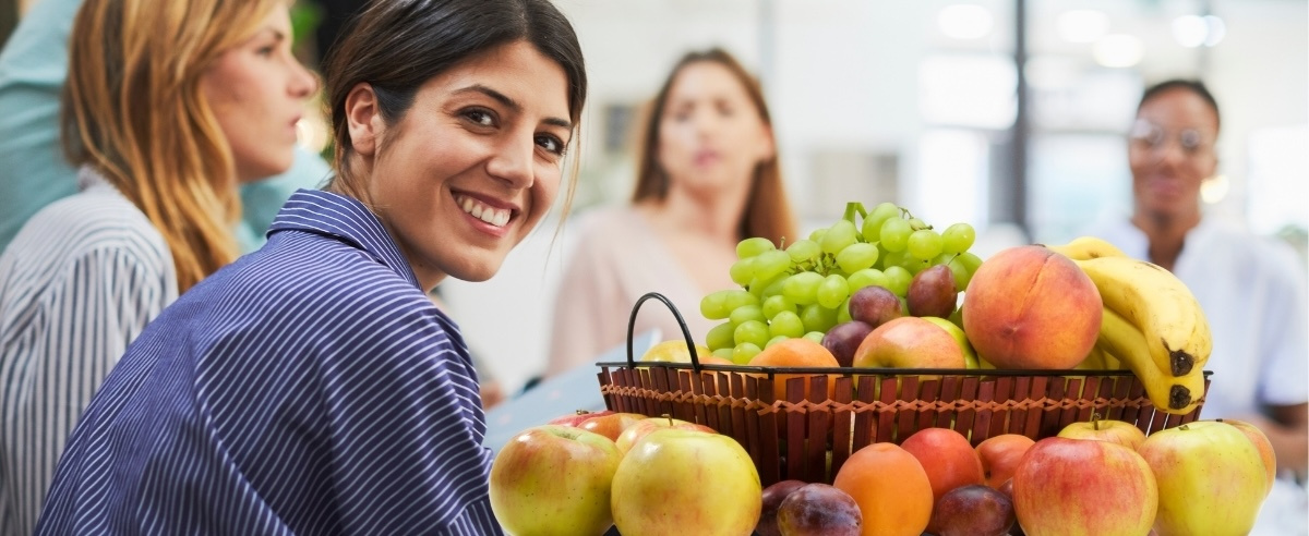 KI generiert: Frau vor Korb mit verschiedenen Früchten, im Hintergrund unscharfe Personen.