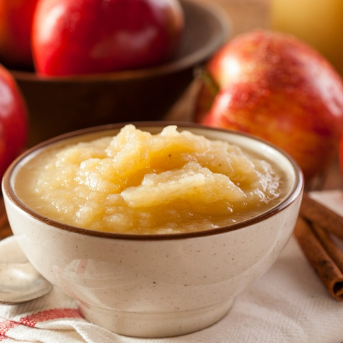 KI generiert: Eine Schüssel Apfelmus mit frischen Äpfeln im Hintergrund.