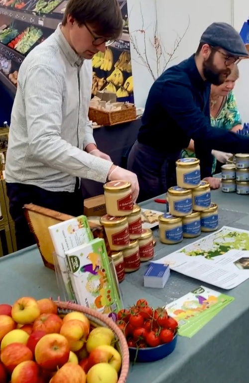 KI generiert: Menschen präsentieren Produkte auf einem Marktstand mit eingelegten Lebensmitteln und frischem Obst.