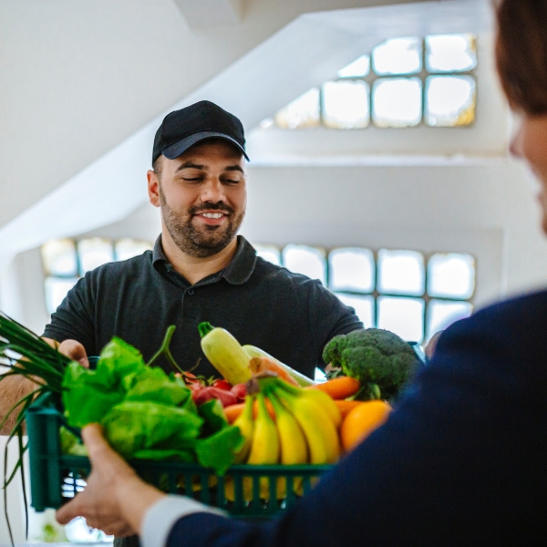 KI generiert: Ein Mann übergibt einer Person eine Kiste voller frischem Obst und Gemüse.