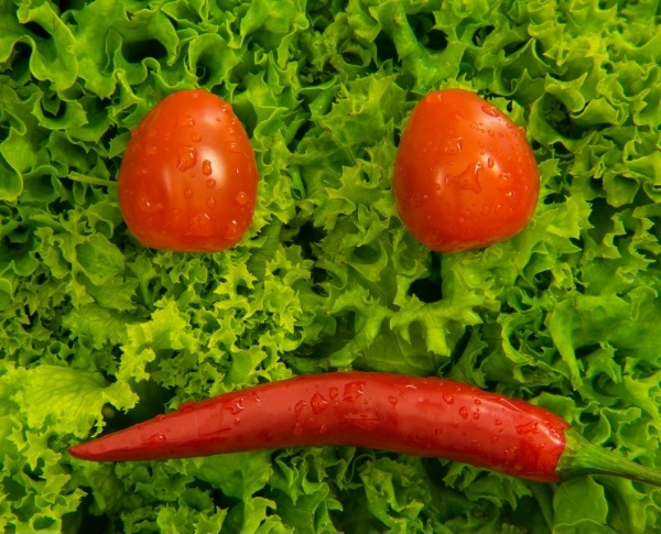KI generiert: Tomaten und Chili in Form eines traurigen Gesichts auf grünem Salat.