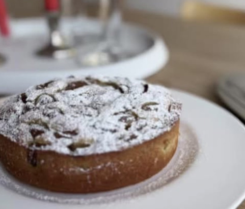 KI generiert: Ein Kuchen mit Puderzucker auf einem Teller, im Hintergrund unscharfe Tischdekoration.