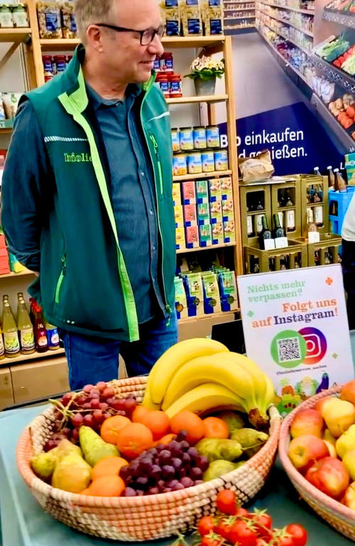KI generiert: Ein Mann steht vor Körben mit Obst in einem Laden. Ein Schild wirbt für Instagram: "Nichts mehr verpassen?"