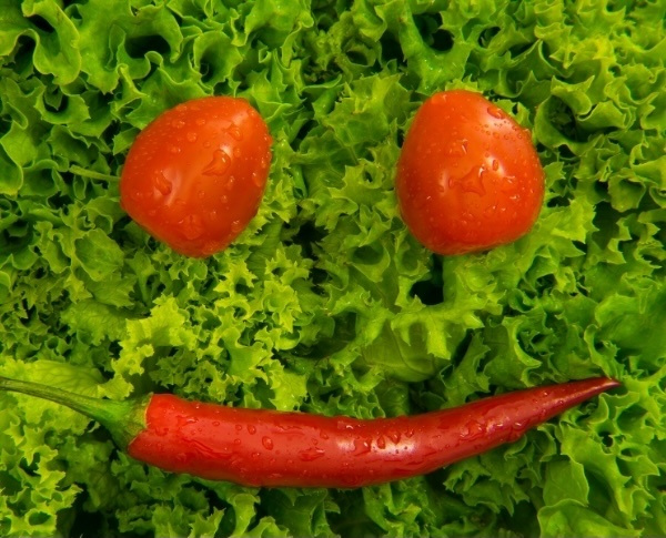 KI generiert: Ein Smiley-Gesicht aus Tomaten und Chili auf grünem Salat.