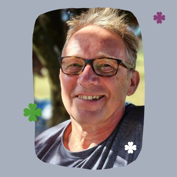 KI generiert: Ein lächelnder Mann mit Brille vor einem unscharfen Hintergrund, umgeben von dekorativen Blumenmotiven.