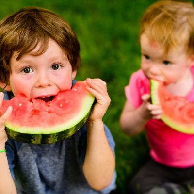 KI generiert: Zwei Kinder essen Wassermelone auf einer Grasfläche.