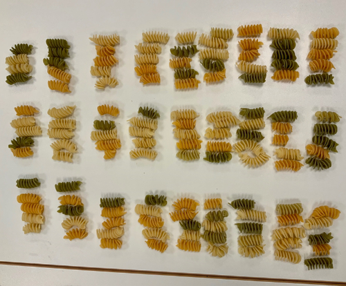 KI generiert: Bunte Fusilli-Nudeln aufgereiht, formen den Satz: "IT NEVER RAINS, BUT IT POURS".