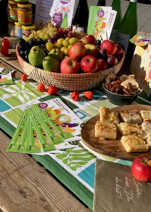 KI generiert: Ein Tisch mit Obsttellern, Gebäck, Getränken und Infokarten. Text: "Schön, dass Du da bist!"