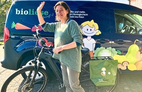 KI generiert: Eine Person lächelt neben einem Lieferwagen und Fahrrad. Text: "bioliese."