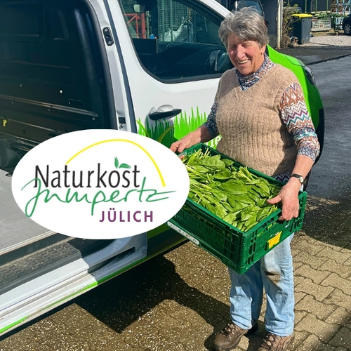 KI generiert: Eine Person trägt eine Kiste mit Spinat. Text: "Naturkost Jülich".