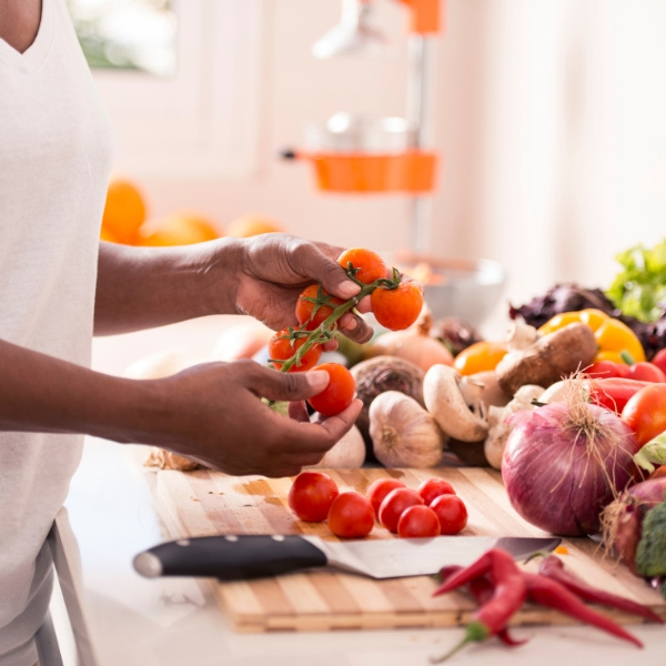 KI generiert: Person wählt frisches Gemüse in der Küche, darunter Tomaten, Pilze und Zwiebeln.