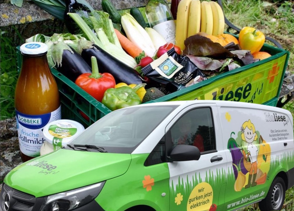 KI generiert: Ein Lieferwagen vor einer Kiste mit frischem Obst und Gemüse. Text: "www.bio-liese.de".